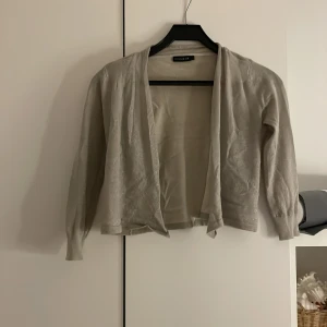 Beige kofta från Stockh LM - Säljer en stilren beige kofta från Stockh LM. Koftan har en öppen design och långa ärmar, perfekt för lager-på-lager. Den är i en neutral färg som passar till det mesta. Perfekt för både vardag och lite finare tillfällen. OBS STOR GALJE