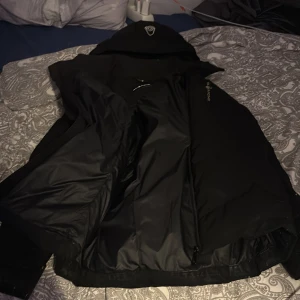 Svart pufferjacka med luva - Säljer en svart pufferjacka med luva. Jackan har en dragkedja framtill och är perfekt för kyligare väder. Den är designad för att hålla dig varm och bekväm. Och jackan är äkta