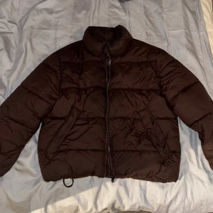 Brun pufferjacka - Säljer en brun pufferjacka med dragkedja. Jackan har en quiltad design och långa ärmar, perfekt för kyligare dagar. Den är både stilren och funktionell. Pufferjacka i storlek Large från HM