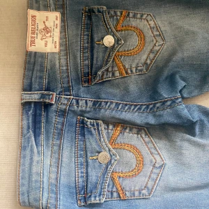 Blå jeans från True Religion - Snygga blå jeans från True Religion med låg midja och flare-stil. De har dekorativa sömmar på bakfickorna och en klassisk femficksdesign. Liten slitning längst ner men inget som märks.