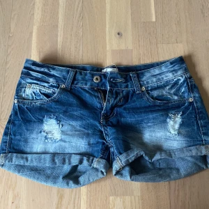 Lågmidjade Blå jeansshorts - Snygga blå jeansshorts med låg midja och  med slitna detaljer och uppvikta ben. Perfekta för en avslappnad stil. De har klassisk femficksdesign och knäppning fram. Köpa i Spanien föra året men har tyvärr vuxit ur dom 