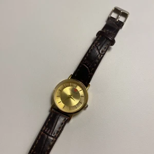 Guldfärgad klocka från Tissot - Elegant Tissot watch with dark brown leather strap and gold details. The watch is in perfect condition. The strap has been a little worn from the inside as you can see in the last picture. 