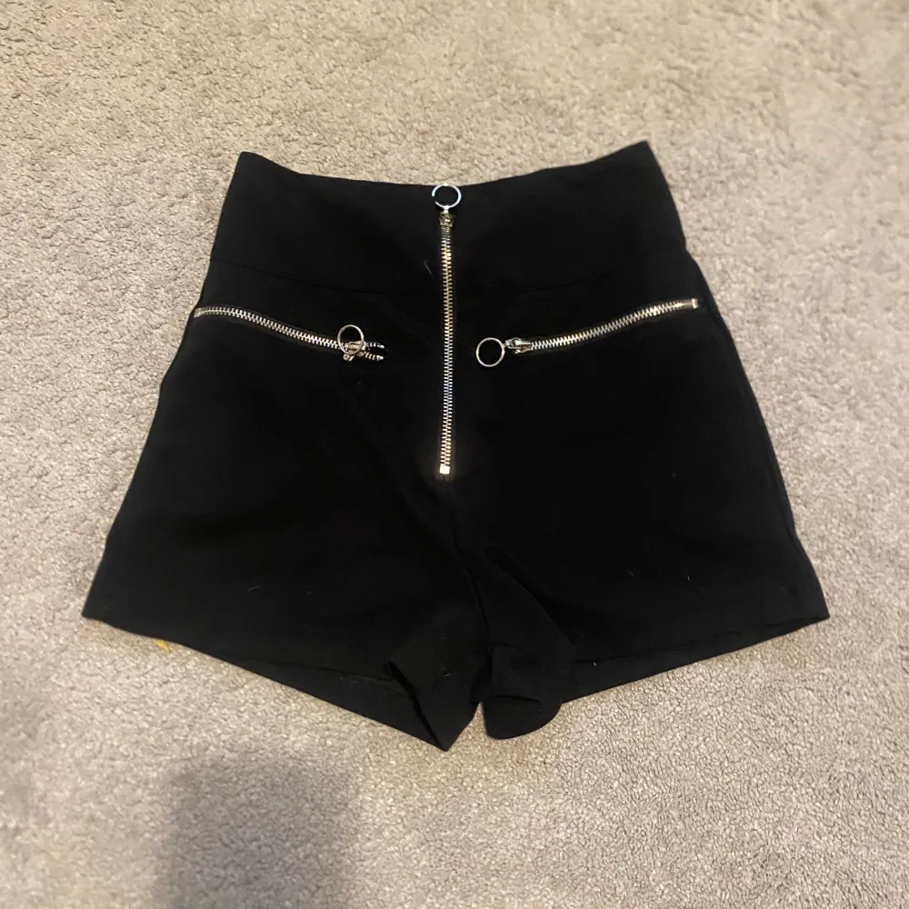 Snygga svarta shorts med hög midja och coola dragkedjor framtill. Perfekta för en trendig look, dessa shorts har en stilren design och passar till många olika outfits.. Shortsit.