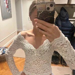 Vit spetsblus - Säljer en elegant vit spetsblus med långa ärmar och v-ringad design. Perfekt för en stilren look med fina detaljer i spetsmönster. Passar bra till både jeans och kjol.