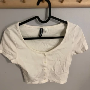 Vit bolero från H&M - Säljer en vit bolero från HM Divided med korta ärmar och knappar framtill. Går att ha både stängd och öppen. Toppen är i ett mjukt material och har en rund halsringning. Perfekt att ha som den är eller med ett linne under. Aldrig använd. Pris kan diskuteras!🥰