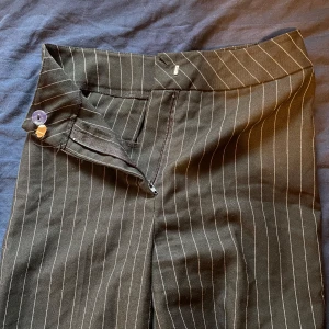 Svarta randiga kostymbyxor - Snygga svarta kostymbyxor med vita ränder. De har en otrolig passform med dragkedja och knapp framtill. Perfekta för en stilren look.