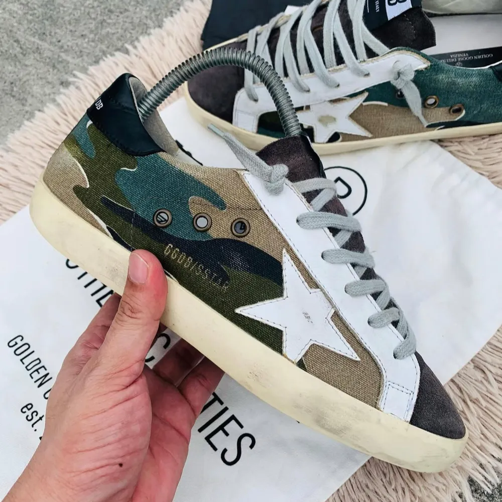 Snygga sneakers från Golden Goose med ett coolt camouflage-mönster i grönt, beige och blått. Skorna har en vit stjärna på sidan och grå snörning. Perfekta för en avslappnad stil med en touch av unik design. Storlek 39 passar 40-41.. Kengät.