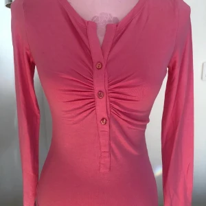 Rosa långärmad topp från Ilse Jacobsen - Snygg rosa långärmad topp från Ilse Jacobsen med knappar framtill och rynkdetalj vid bysten. Perfekt för en stilren look.
