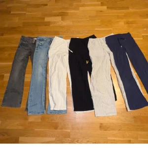 Samling av olika byxor - En samling av sex olika byxor i varierande färger och stilar. Inkluderar jeans i grått och ljusblått, vita och svarta byxor samt randiga och mörkblå byxor. Perfekt för att variera garderoben med olika passformer och material. En liten fläck befinner sig på den vita linnebyxan.
