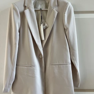 Oanvänd Beige kavaj från Neo Noir  - Elegant beige kavaj från Neo Noir med klassisk design och enkel knapp framtill. Perfekt för en stilren look. Kavajen har en tidlös passform och är tillverkad i ett mjukt material.