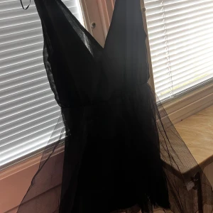 Svart klänning från Sally&Circle - Snygg svart klänning från Sally&Circle med v-ringad design och transparenta detaljer. Perfekt för en kväll ute eller en speciell tillställning. Klänningen har en elegant och stilren look.