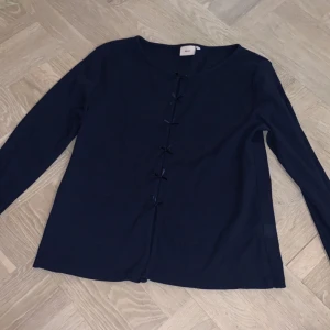 Mörkblå tröja från Nelly - Säljer en stilren mörkblå tröja från Nelly med rosetter framtill. Tröjan har långa ärmar och en rund halsringning. Perfekt för en avslappnad look.