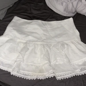 Vit kjol från Zara - Säljer en söt vit kjol från Zara med volangdetaljer och spetskant. Perfekt för sommarens varma dagar. Kjolen har en kort längd och är tillverkad i ett lätt och luftigt material. Jag har aldrig andvänt den!