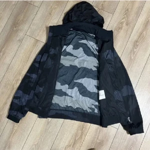 Camouflagejacka från Moncler - Säljer en snygg camouflagejacka från Moncler. Jackan har en cool design med huva och dragkedja. Perfekt för dig som vill ha en stilren look med en touch av edge. Den är långärmad och har ett märke på ärmen.