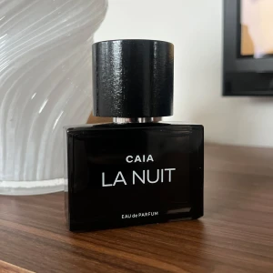 CAIA La Nuit Eau de Parfum 50 ml - Elegant och mystisk parfym från CAIA, La Nuit, i en stilren svart flaska med en minimalistisk design. Flaskan har en fyrkantig form med en stor, rund svart kork. Perfekt för den som vill ha en sofistikerad doftupplevelse. 