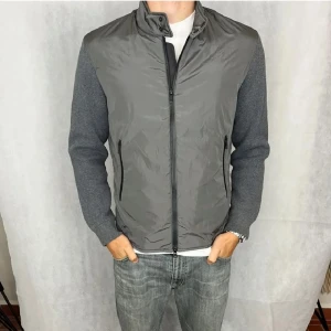 Grå cardigan från Massimo Dutti - Snygg grå cardigan från Massimo Dutti med dragkedja och ståkrage. Ärmarna är i ett mörkare grått tyg som ger en fin kontrast. Perfekt till våren. Modellen på bilden är 183 cm. Pris går att diskuteras vid snabb affär