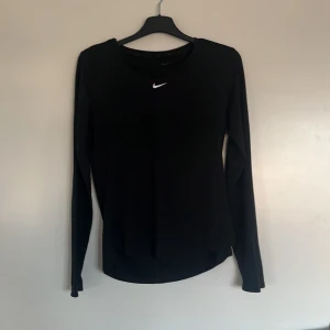 Svart långärmad tränings tröja från Nike - Säljer en svart långärmad tröja från Nike med Dri-FIT-teknologi. Perfekt för träning med sin bekväma passform och fukttransporterande material. Den har en liten Nike-logga på bröstet. Passar bra för aktiva dagar!