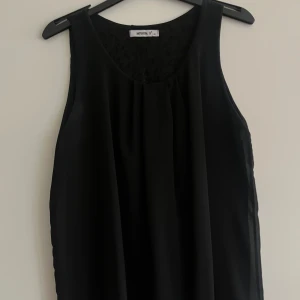 Svart ärmlös topp från MyHailys - Snygg svart ärmlös topp från MyHailys med en elegant öppen ryggdetalj. Perfekt för en stilren look. Tillverkad i ett lätt och luftigt material som ger en skön passform.