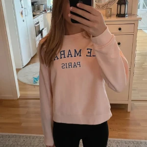 Ljusrosa sweatshirt från Lindex - Säljer en ljusrosa sweatshirt från Lindex med trycket 'LE MARAIS PARIS' i blått på framsidan. Tröjan har långa ärmar och en rund halsringning. Perfekt för en avslappnad stil.