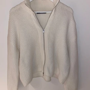 Vit stickad kofta från BikBok - Säljer en stilren vit stickad kofta från BikBok med dragkedja framtill. Koftan har en ribbad struktur och långa ärmar, perfekt för kyligare dagar. Passar bra till både jeans och kjol.