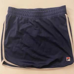 Mörkblå tenniskjol från Fila - Snygg mörkblå kjol från Fila med vita kantdetaljer. Perfekta för sportiga aktiviteter. Elastisk midja för bekväm passform.