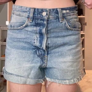 Blå jeansshorts - Snygga blå jeansshorts med hög midja och knappgylf. De har en avslappnad passform med fransiga kanter för en cool look. Perfekta för sommardagar!