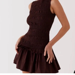 Peppermayo klänning  - Snygg brun ärmlös klänning med smockdetaljer och volangkant. Perfekt för en stilren look med en kort och lekfull kjol. Pris går att diskutera!