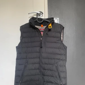 Svart dunväst från Parajumpers - Säljer en svart dunväst från Parajumpers. Västen är superlätt och har en dragkedja framtill. Den är perfekt för mellanvarma dagar och har en stilren design med märkets logga på baksidan. Jag säljer den då den inte passar mig och har då ingen användning av den.