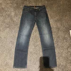 Blå jeans från Lee - Snygga blå jeans från Lee med klassisk femficksdesign och knappgylf. W31 L32