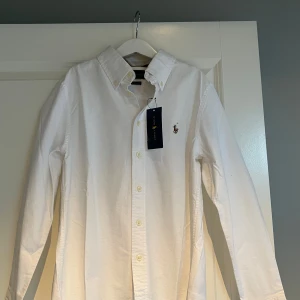 Vit skjorta från Ralph Lauren - Säljer en klassisk vit skjorta från Ralph Lauren.  Skjortan har långa ärmar och knappar framtill. Perfekt för en stilren look. 🕴️pris kan diskuteras,tveka inte att höra av er om frågor storleken är 10 till 12 år 