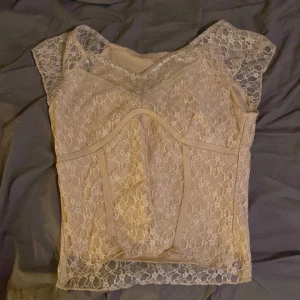 Beige spets topp - Elegant beige topp med vacker spetsdesign. Den har en v-ringad hals och korta ärmar, vilket ger en romantisk känsla. Perfekt för att lägga till en touch av elegans till din outfit.