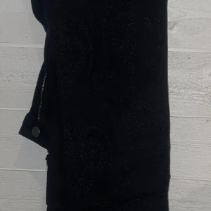 Svarta lågmidjade byxor med broderade detaljer från Odd Molly - Snygga svarta byxor från Odd Molly med unika broderade mönster. Byxorna har en dragkedja och knappdetalj. Perfekta för att ge en stilfull touch till din outfit. 