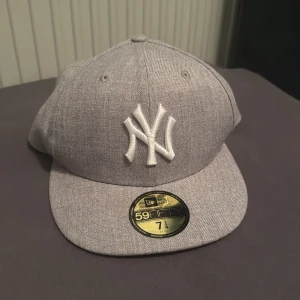Grå keps från New Era - Snygg grå keps från New Era med broderad logga framtill. Klassisk 59FIFTY-modell med platt skärm och bekväm passform. Perfekt för en stilren look.