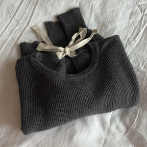 Mörkgrå stickad tröja från Zara - Mörkgrå stickad tröja från Zara. Den är ribbad och har en dekorativ knytning i nacken. Aningen nopprig men fortfarande fin, därav pris.
