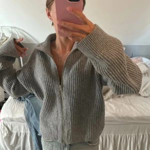 Grå stickad kofta med dragkedja - Mysig grå stickad kofta med dragkedja framtill. Perfekt för kyliga dagar med sin ribbade struktur och långa ärmar. En stilren och bekväm tröja som passar till det mesta.