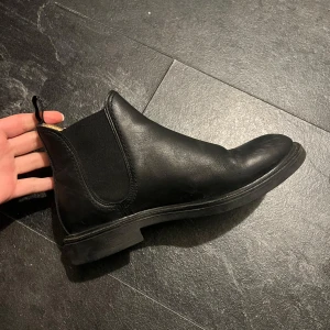 Svarta Chelsea boots från Stockholm Design - Snygga svarta Chelsea boots i skinn från Stockholm Design. De har en klassisk design med elastiska paneler på sidorna för enkel på- och avtagning. Perfekta för både vardag och mer uppklädda tillfällen.