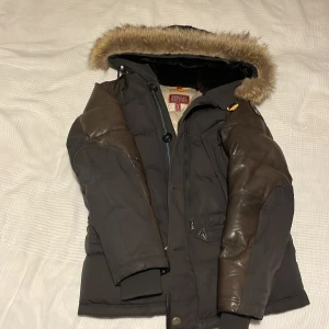Svart dunjacka från Parajumpers - Säljer en svart Parajumpers Special Edition dunjacka med pälsdetaljer på huvan. Jackan har långa ärmar och en kombination av knappar och dragkedja framtill. Perfekt för kalla dagar med sin varma och skyddande design. PRIS KAN DISKUTERAS!!