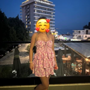 Blommig kortklänning med volanger - Charmig blommig kortklänning i rosa och vit med volanger. Axelbandslös design. Använd endast en gång. Från shein 