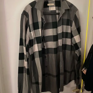 Rutig skjorta från Burberry - Snygg rutig skjorta från Burberry i grå och svart. Skjortan har långa ärmar och knappar framtill. Perfekt för en stilren look.