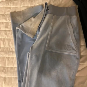 Ljusblå mjukisbyxor med snörning - Säljer ett par ljusblå mjukisbyxor med snörning i midjan och fickor framtill. Byxorna har en broderad logga på ena fickan och är perfekta för en avslappnad stil. De är lite slitna nertill men sitter skit snyggt på kan visa bild om det önskas