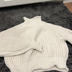 Vit stickad polotröja - Mysig vit stickad polotröja med hög krage och långa ärmar. Perfekt för kyliga dagar och ger en stilren look. Tröjan har en grovstickad design som ger extra värme och komfort.