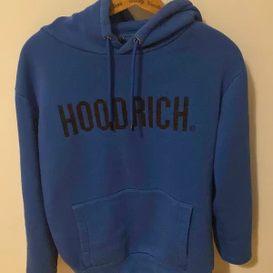 Blå hoodie från Hoodrich - Säljer en snygg blå hoodie från Hoodrich med svart text på bröstet. Den har en klassisk känguruficka och justerbar huva med dragsko. Perfekt för en avslappnad stil.kvalitet 7/10 pris kan diskuteras 