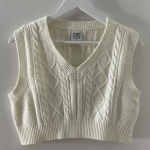 Vit stickad väst från BDG - Säljer en snygg vit stickad väst från BDG med kabelstickat mönster och v-ringning. Använd två  gånger bara ser ut som ny.  🧶✨