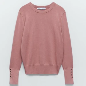 Rosa tröja från Zara - Säljer en rosa tröja från Zara med rund hals och långa ärmar. Tröjan har dekorativa knappar vid ärmsluten och är perfekt för en stilren look. Observera att det finns ett litet hål vid axeln.