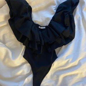 Svart volang body zara - Elegant svart body med stora volangdetaljer över axlarna och bröstet. Perfekt för en stilren look.