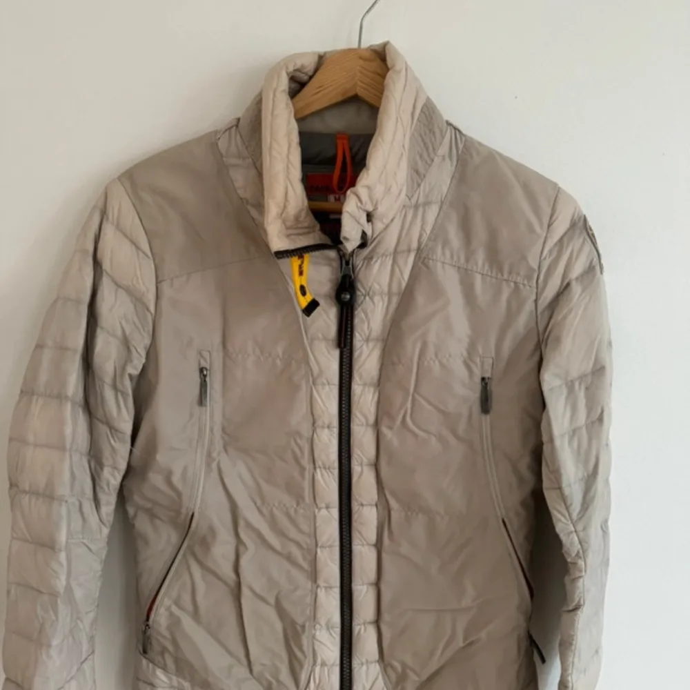Säljer en snygg beige dunjacka från Parajumpers med dragkedja och hög krage. Jackan har långa ärmar och praktiska fickor med dragkedja. Är i fint skick!. Takit.
