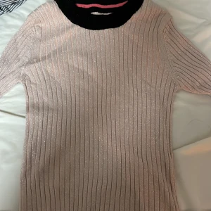 Glittrig ribbad tröja - Snygg glittrig tröja i en ljusrosa nyans med ribbad struktur. Tröjan har långa ärmar och en tight passform, perfekt för att ge lite extra glam till din outfit.