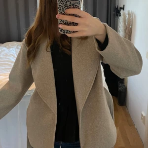 Beige kappa från ONLY - Säljer en stilren beige kappa från ONLY i återvunnen polyester. Kappan har en elegant design med knytbälte i midjan och långa ärmar. Perfekt för höst och vår, den är aldrig använd så den är in köpt för ny pris 💓