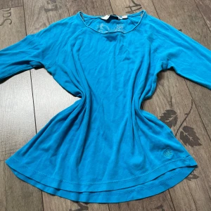 Blå tröja  - Säljer en snygg blå tröja. Tröjan har lång armar och ett diskret broderat märke på framsidan. Perfekt för en avslappnad stil.