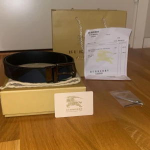 Svart och blått bälte från Burberry - Nytt buberry bälte som används ändast 1 gång. Den är i ett helt nytt skick och man får även med påse, låda och ett burberry kort. Bältet används inte längre och därför har jag valt att sälja den. Ett jätte fint bälte i färgen blått med svarta detaljer.